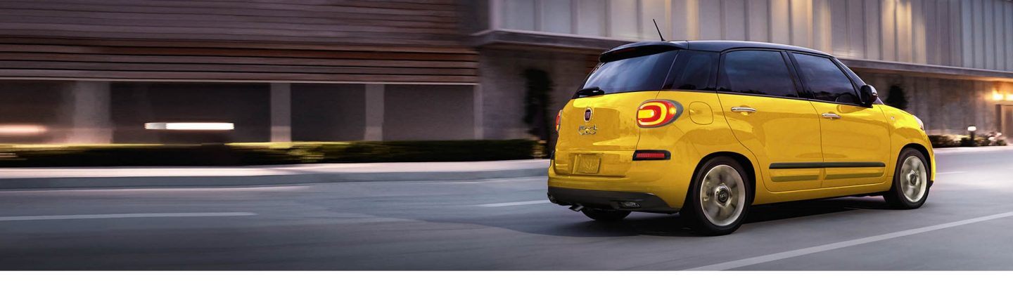 A rear profile view of a 2020 Fiat 500L Trekking being driven on a city street.