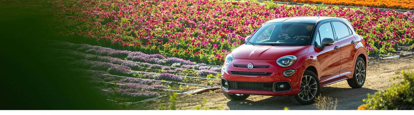 A red 2020 Fiat 500X Sport on a dirt road beside a field of flowers.