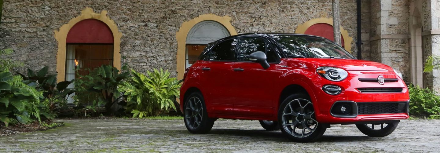 A three-quarter side view of a red 2020 Fiat 500X Sport parked on a cobblestone road.